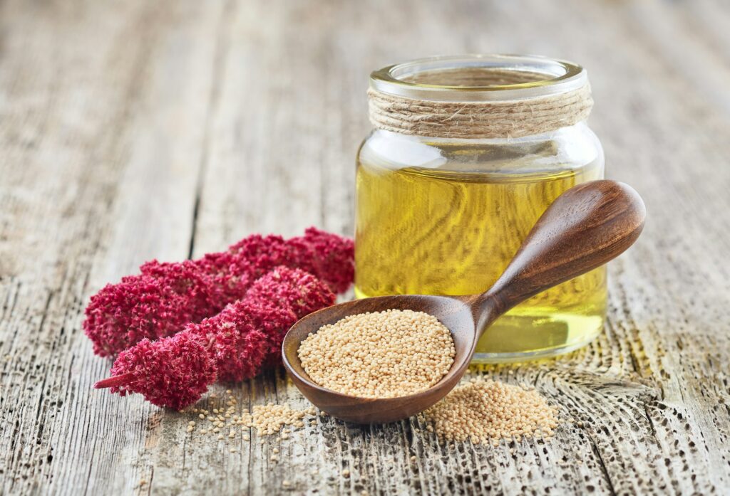 Amaranth oil with plant and seeds on wooden background