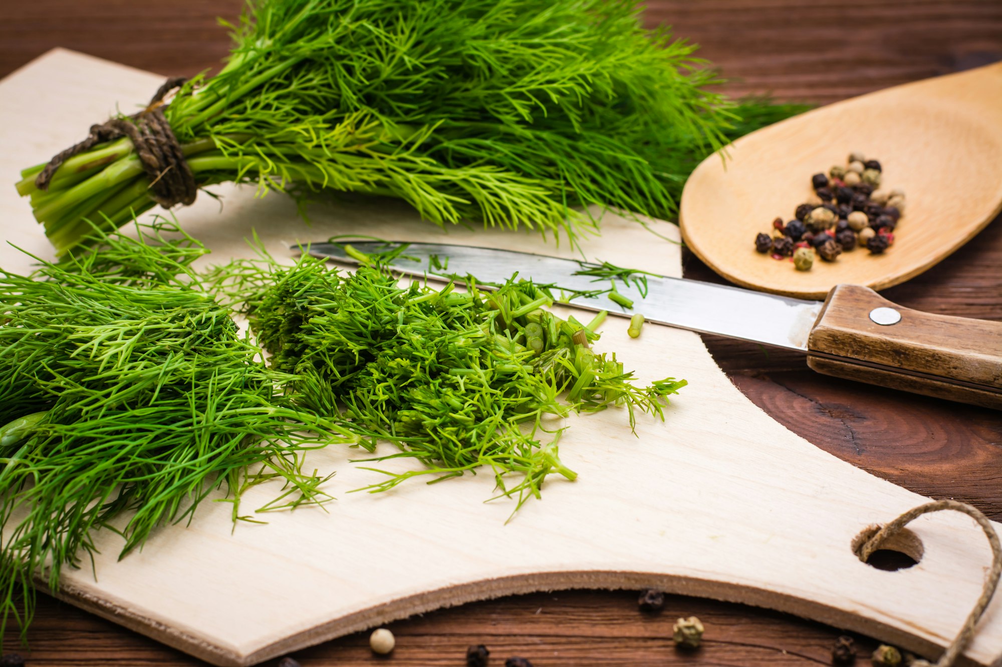Chopped fresh dill on a cutting Board and a bunch of dill on a wooden table