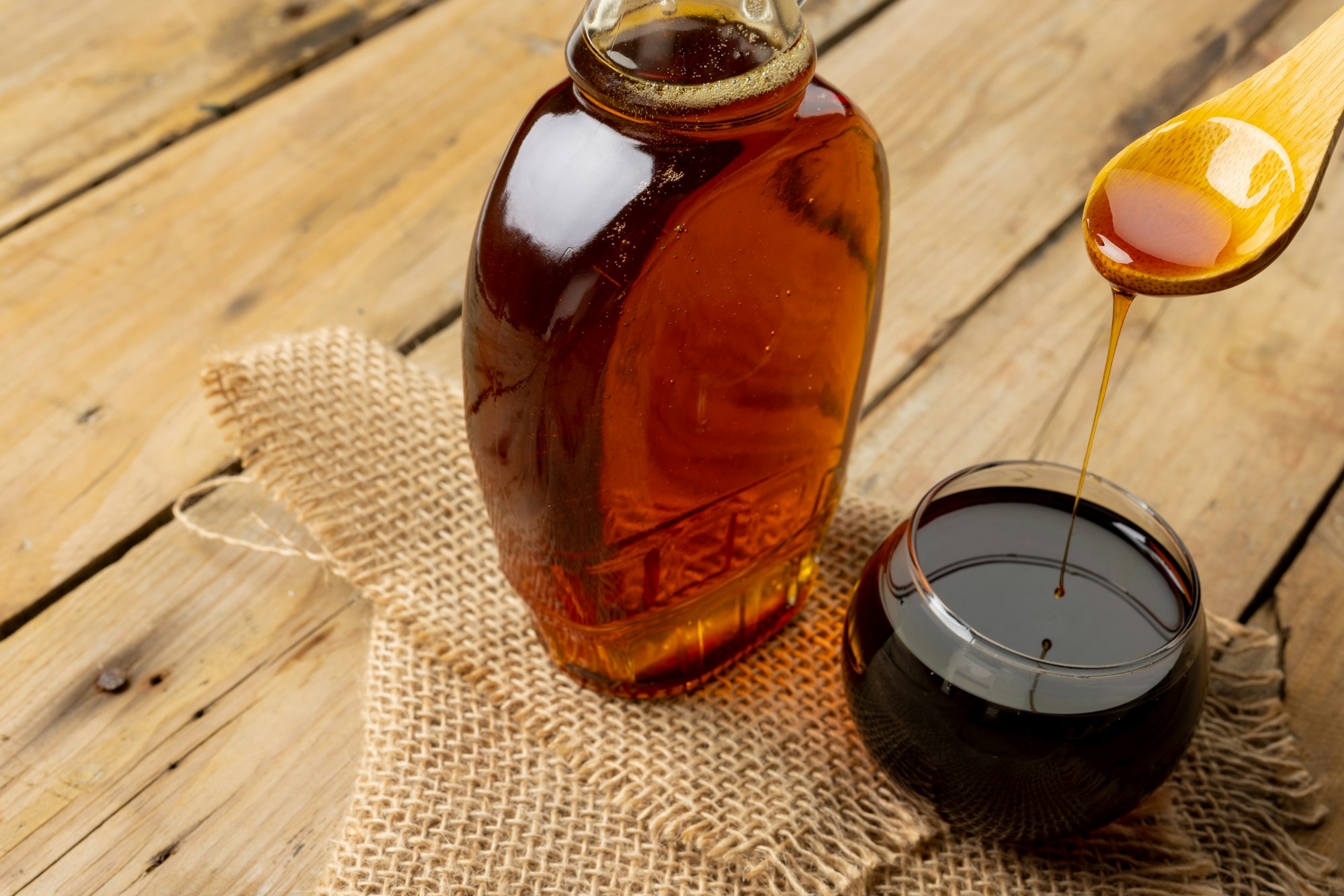 Horizontal image of bottle, wooden spoon and bowl of maple syrup on sackcloth and wood, copy space