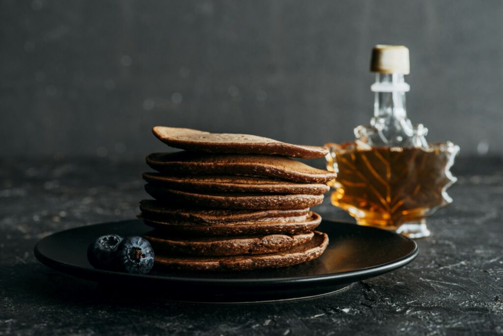 15 Sweet Facts About Maple Syrup You Never Knew 2 stacked chocolate pancakes with bottle of maple syrup